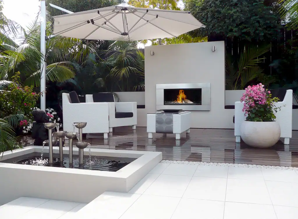 Herne Bay outdoor living area with fireplace, stainless steel water feature and lush tropical palms.