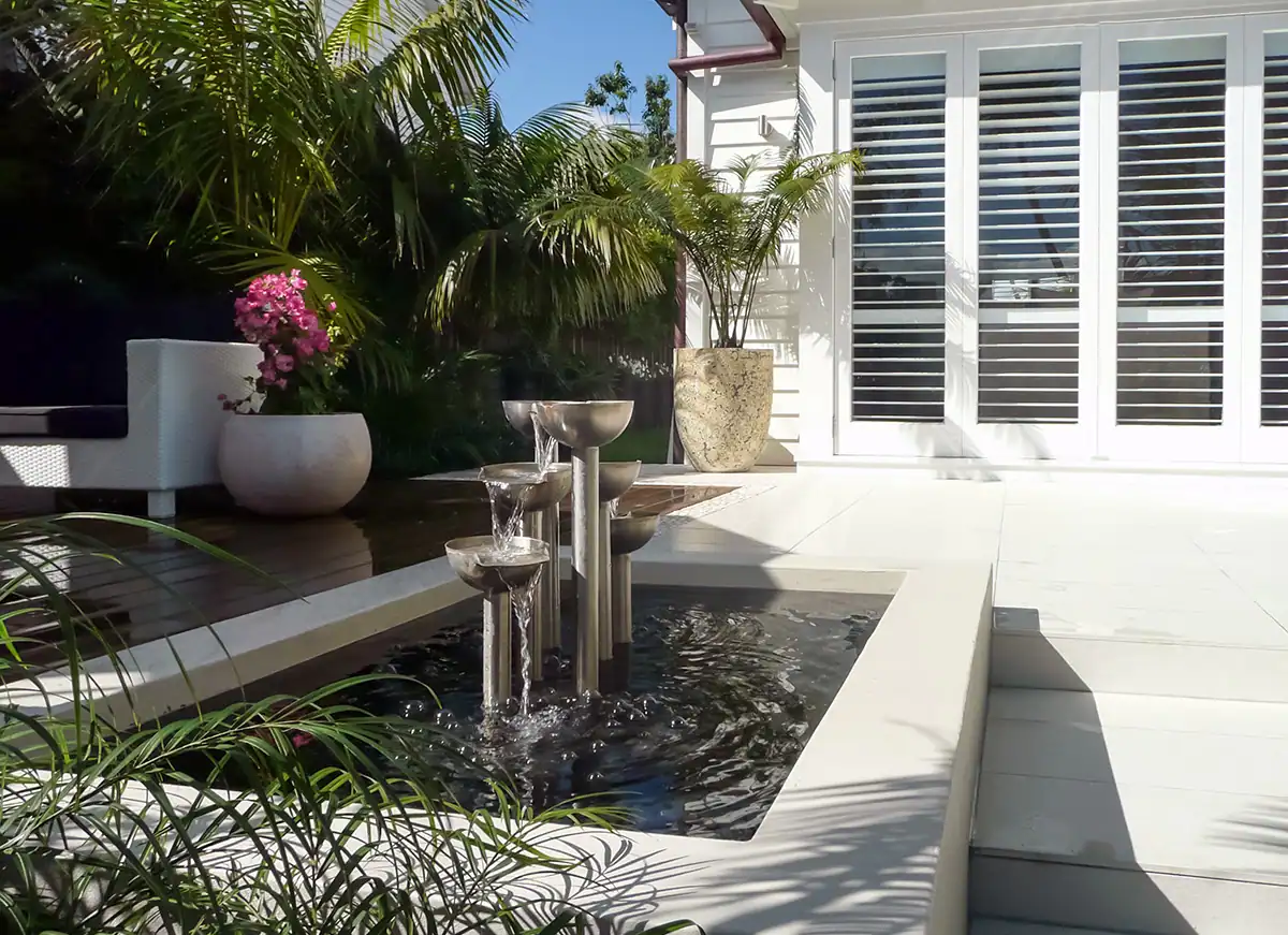 Modern stainless steel water feature and tiled entrance with deck in Herne Bay garden.
