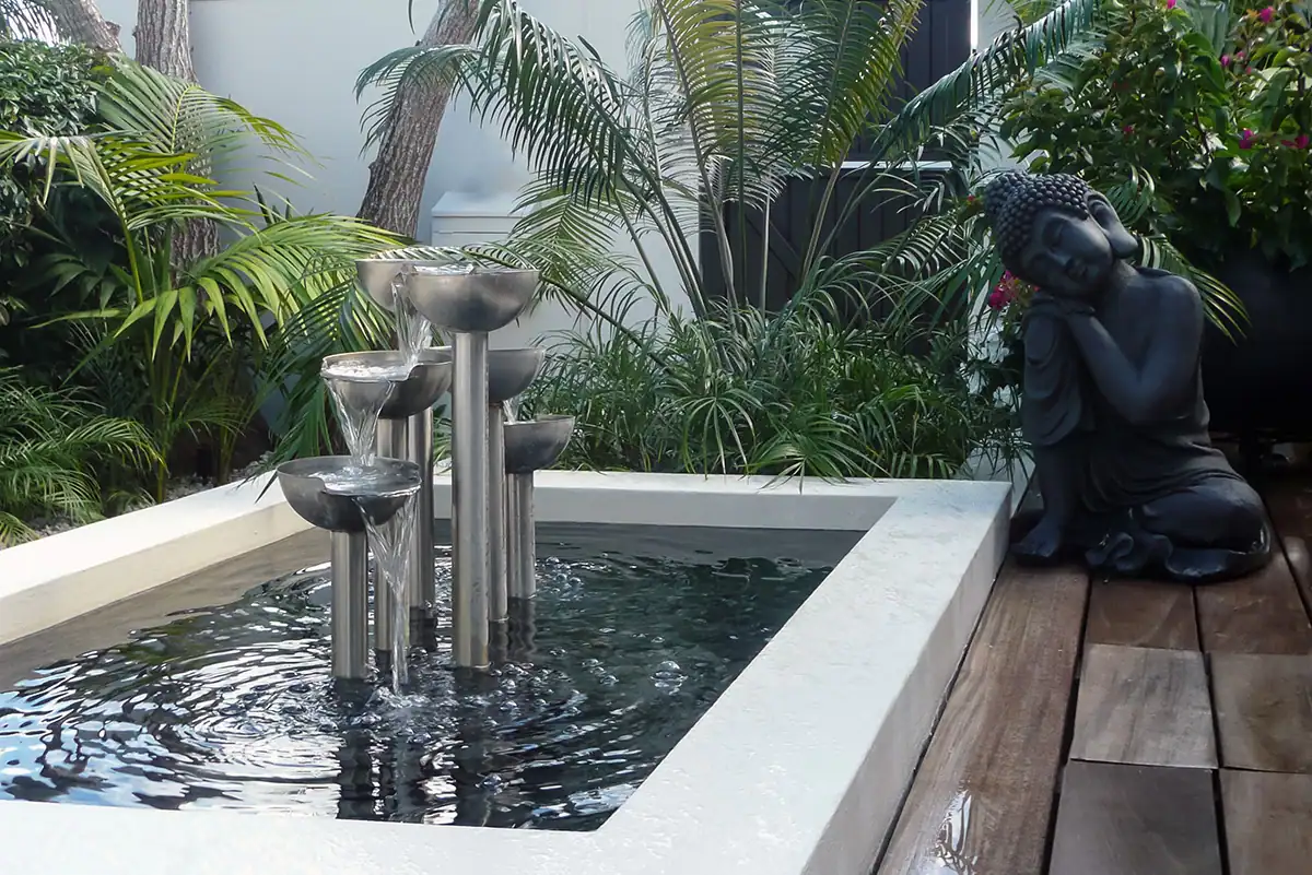 Herne Bay private garden with tiled patio, outdoor fireplace, and tropical palms.