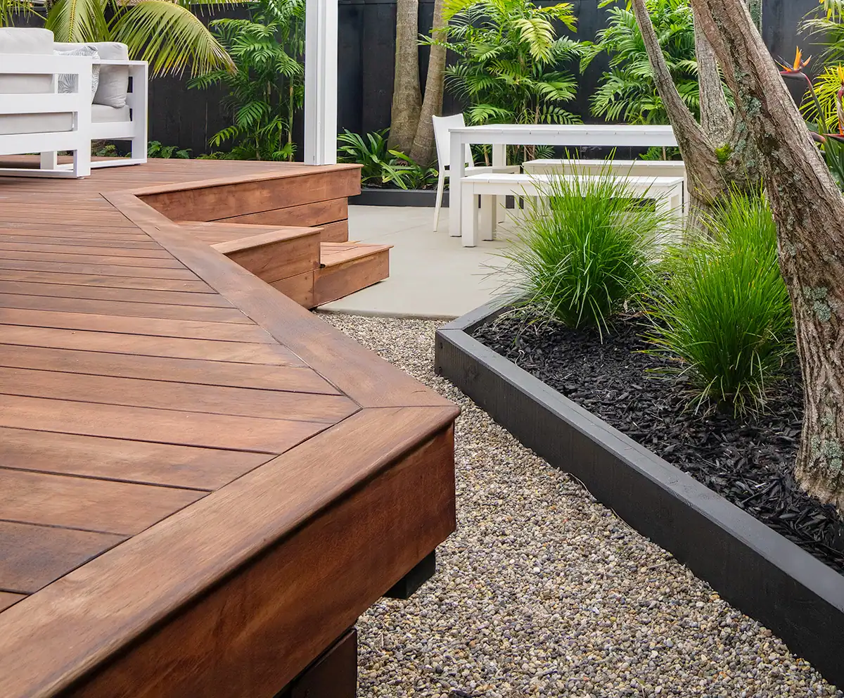 Timber deck and steps leading to corner seating area with raised garden beds with mixed tropical plants in Auckland garden designed by Flourish Garden Concepts