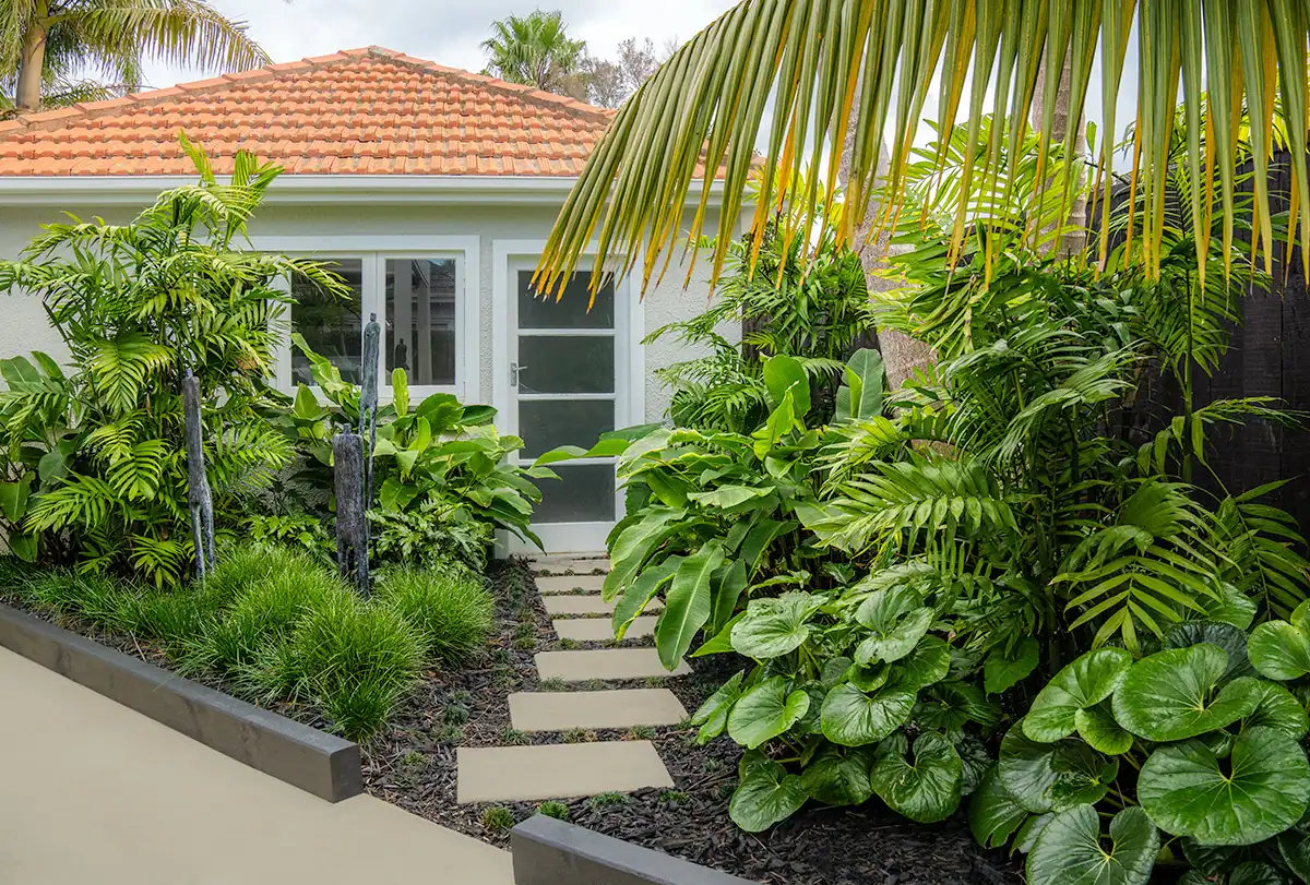 Milford tropical garden featuring lush tropical plants, bronze sculptures and stepping stones leading to garage.