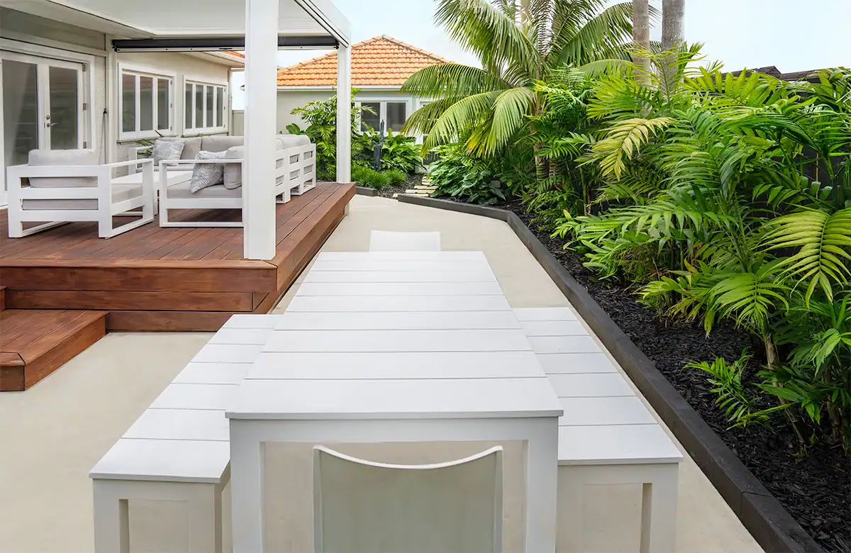 Outdoor seating beneath louvre pergola surrounded by lush tropical planting.