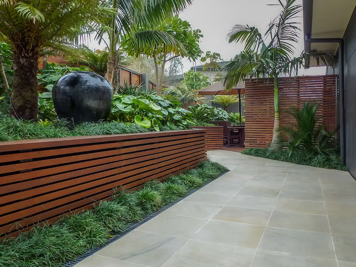 Tiled entrance path leading to private seating area in Birkenhead featuring a large Balinese feature pot and layered foliage plants.