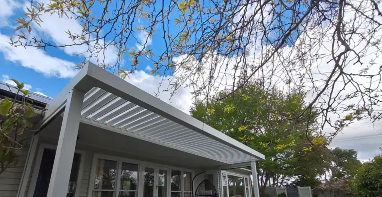 White louvre pergola over outdoor lounge seating area.